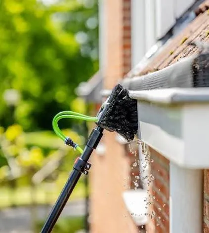 Brush on a water-fed pole cleaning a white uPVC gutter and fascia board